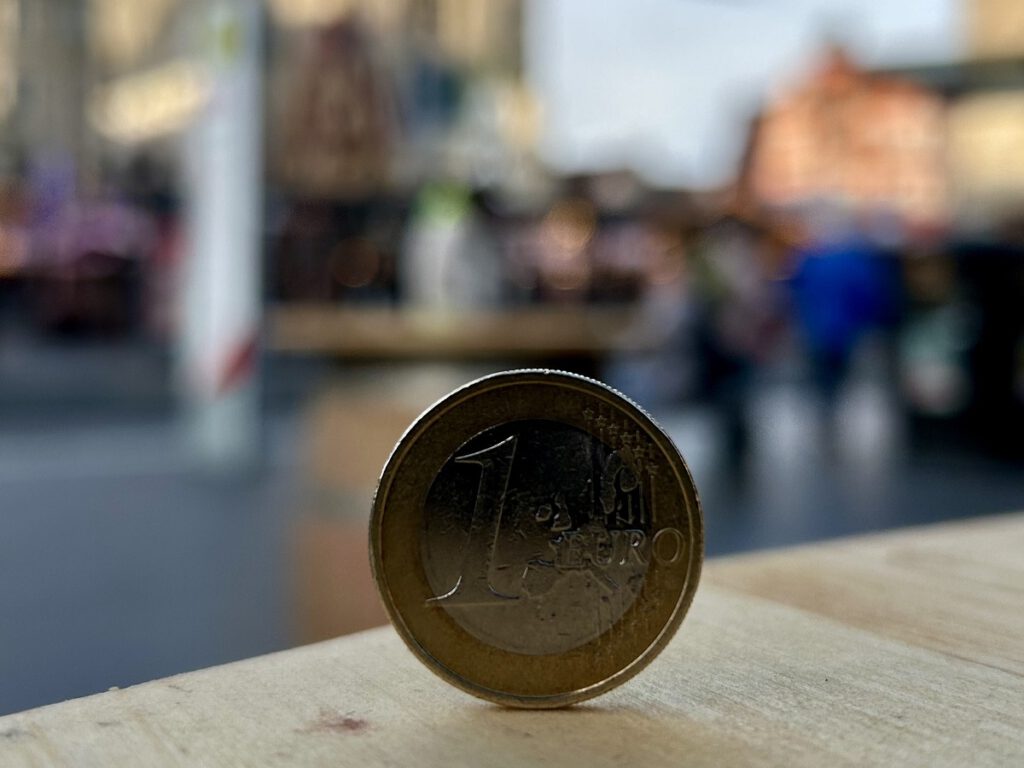 Auf der Seite stehende Euromünze vor unscharfem Blick auf den Marktplatz